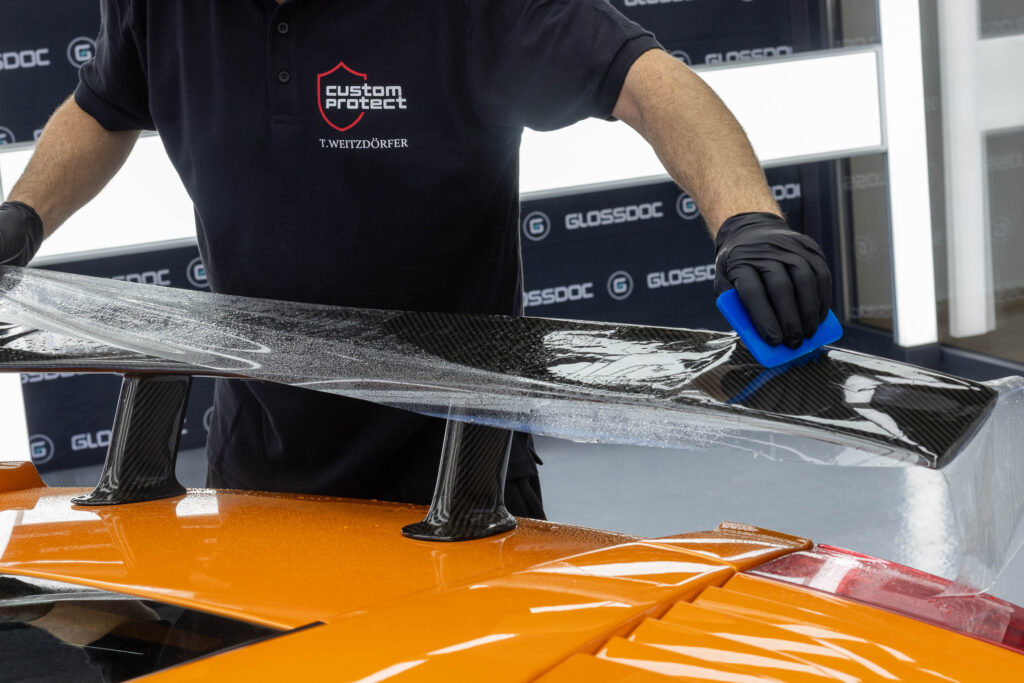 Aufziehen von PPF Schutzfolie auf Heckspoiler von orangenem Lamborghini