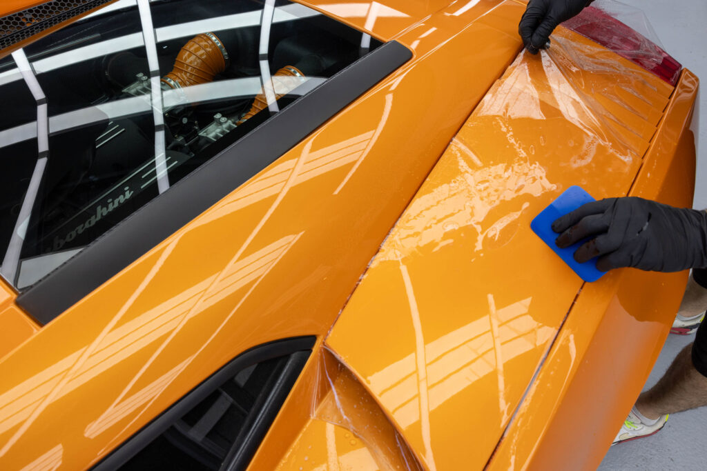 Aufziehen von PPF Schutzfolie auf Kotflügel von orangenem Lamborghini